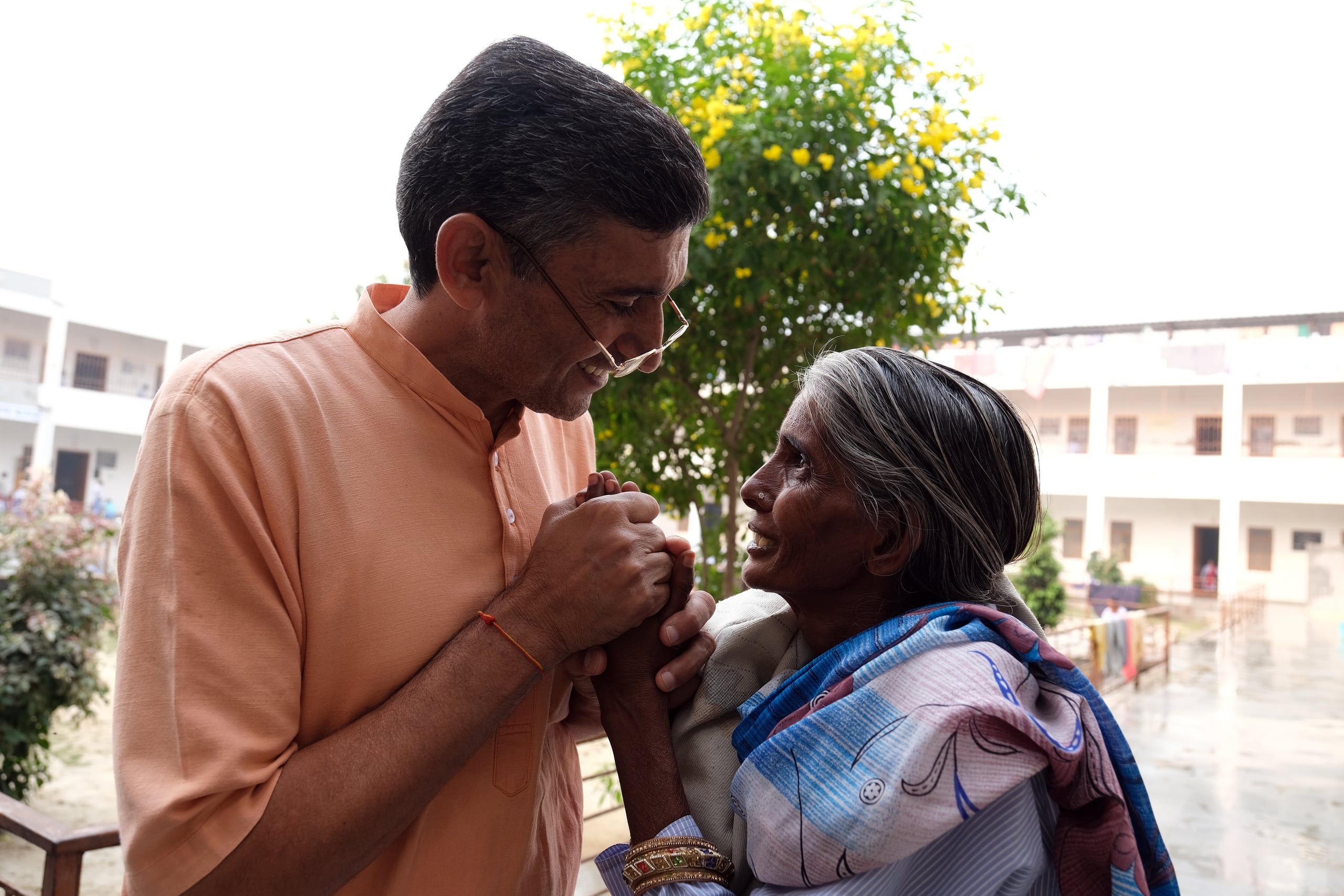 A society member warmly clasps the hands of an elderly woman during a field assignment